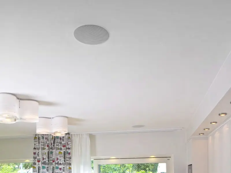 Round white in-ceiling speaker in a bright living room